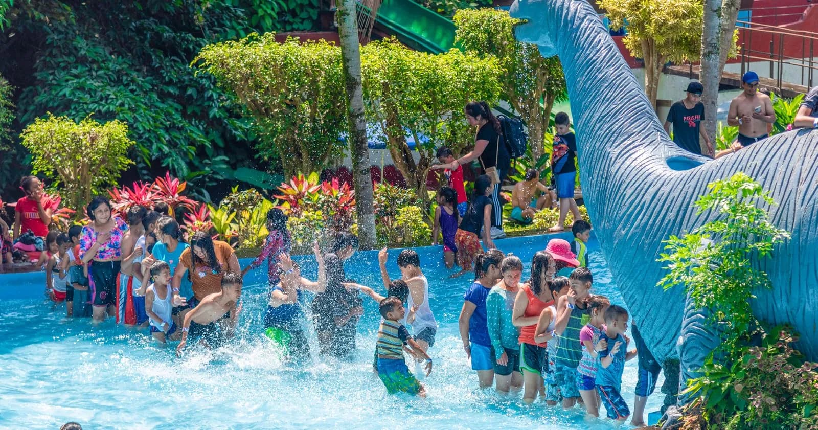 Grupo de niños salpicando agua junto al dinosaurio del parque