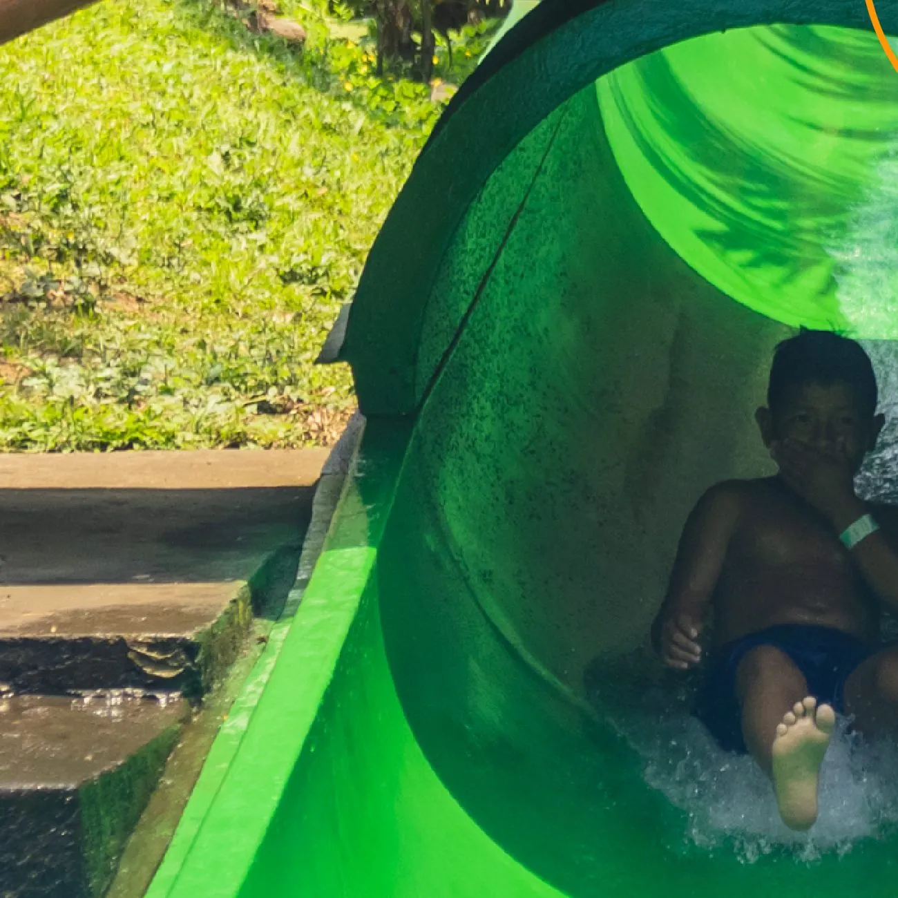 Niño saliendo del tobogán de tubo verde a la piscina